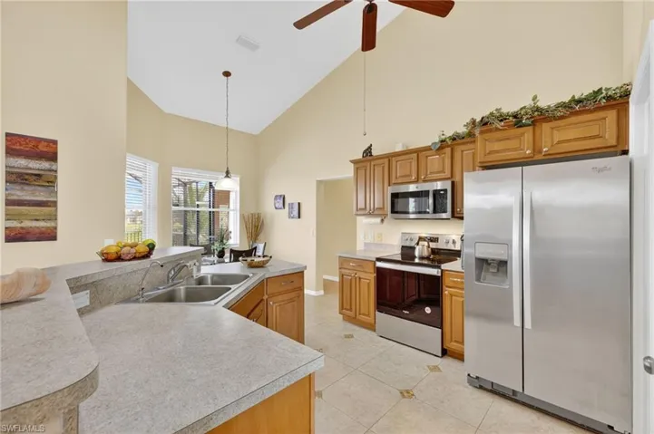Kitchen featuring stainless steel appliances, high vaulted ceiling, light tile patterned floors, ceiling fan, and decorative light fixtures