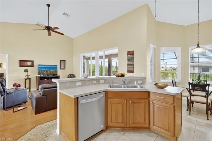 Kitchen with stainless steel dishwasher, high vaulted ceiling, open floor plan, light countertops, and a ceiling fan
