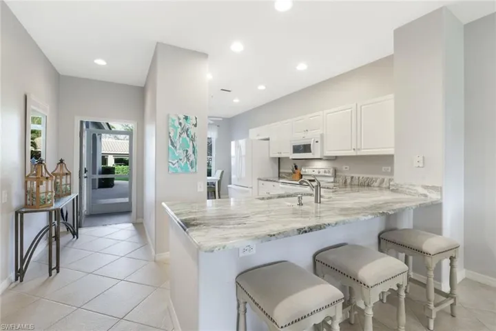 Kitchen featuring white cabinetry, white appliances, light stone countertops, and kitchen peninsula
