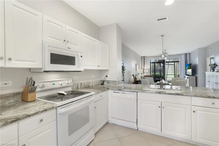 Kitchen with sink, white cabinets, light tile patterned floors, kitchen peninsula, and white appliances