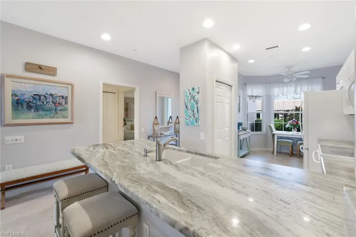 Kitchen featuring sink, a breakfast bar, ceiling fan, stove, and light stone counters