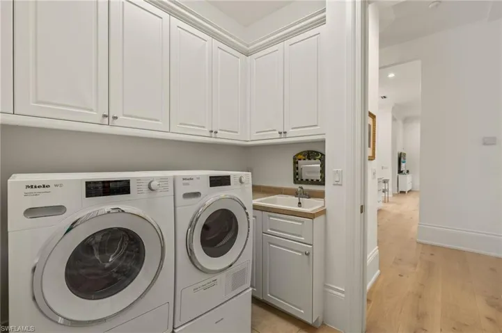 Washroom with cabinets, sink, washing machine and clothes dryer, and light wood-type flooring