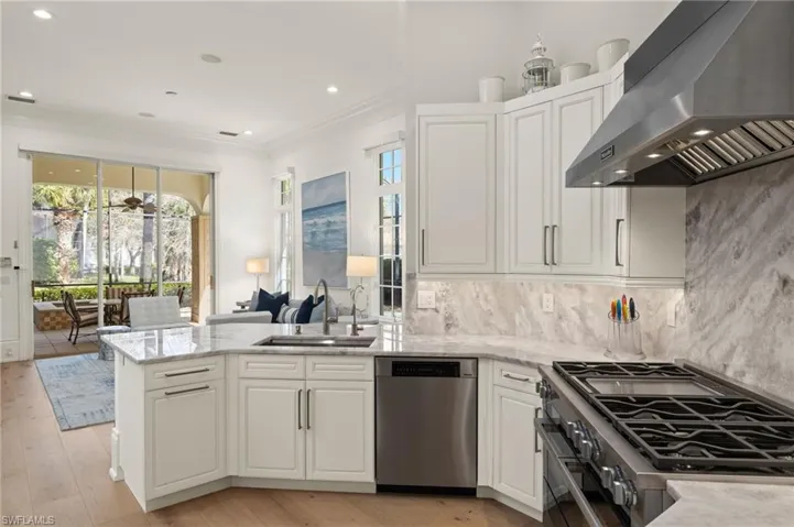 Kitchen with sink, appliances with stainless steel finishes, white cabinetry, light stone counters, and exhaust hood