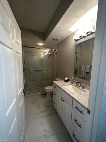 Full bathroom featuring visible vents, vanity, toilet, marble finish floor, and a marble finish shower