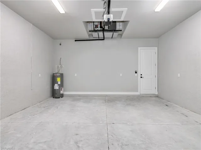 Spacious garage featuring concrete flooring, a water heater, and an overhead garage door opener mechanism