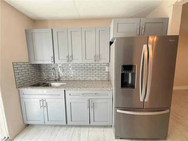 Kitchen with gray cabinetry, stainless steel fridge, light stone countertops, and backsplash