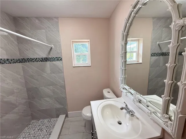 Full bathroom with vanity, light marble finish flooring, healthy amount of natural light, and tiled shower