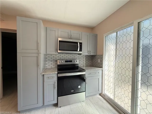 Kitchen with gray cabinets, appliances with stainless steel finishes, light stone countertops, and tasteful backsplash