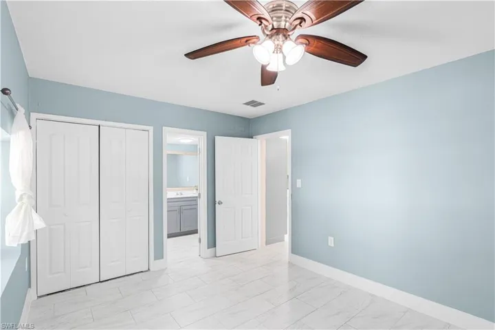 Unfurnished bedroom with a closet, a ceiling fan, light marble finish flooring, and connected bathroom