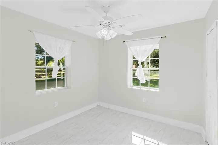 Empty room featuring marble look tiles, plenty of natural light, and ceiling fan
