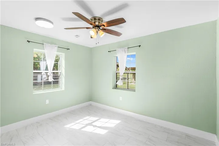 Empty room featuring plenty of natural light, marble look tiles, and ceiling fan