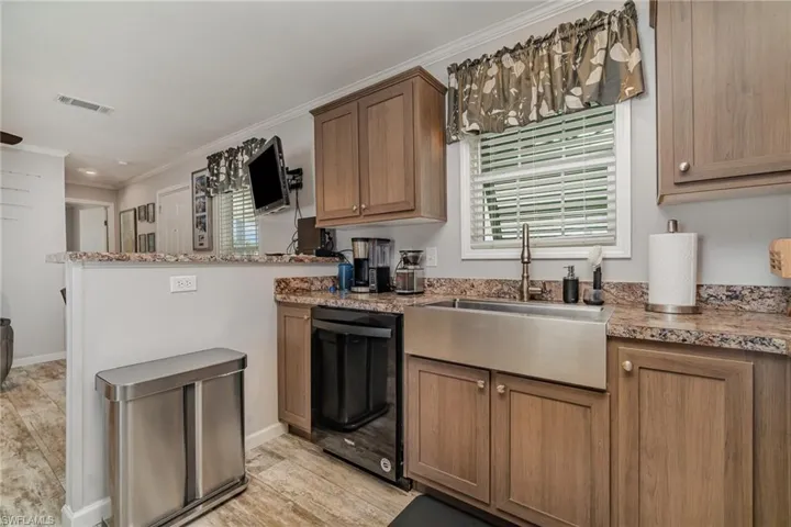 Kitchen with sink, crown molding, light hardwood / wood-style flooring, black dishwasher, and light stone countertops