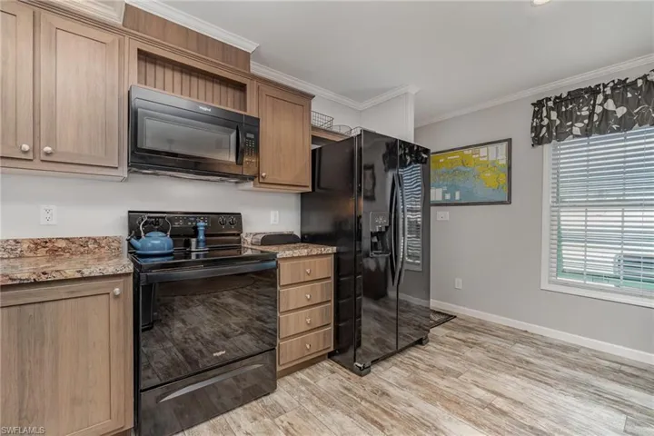 Kitchen with crown molding, light hardwood / wood-style floors, light stone counters, and black appliances