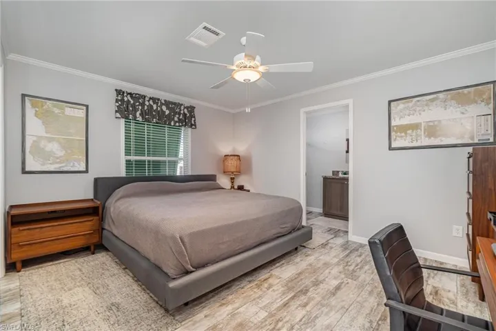 Bedroom with ornamental molding, connected bathroom, ceiling fan, and light hardwood / wood-style flooring