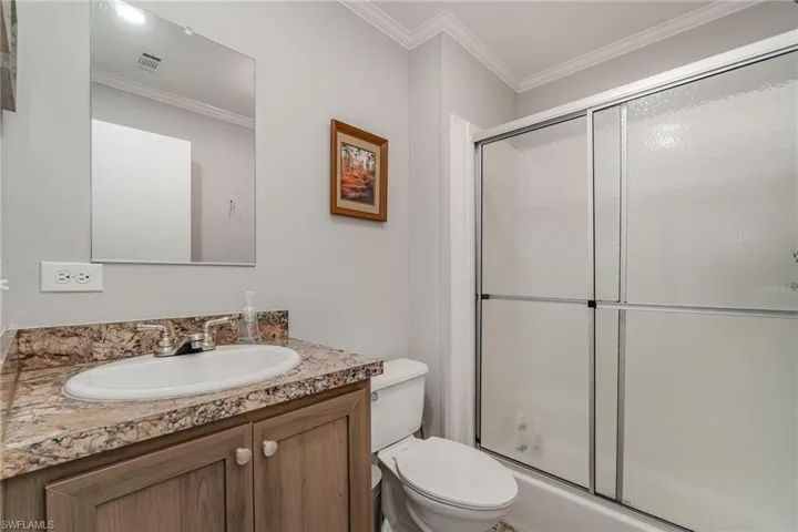 Bathroom featuring crown molding, vanity, toilet, and a shower with door