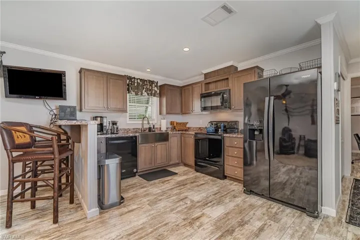 Kitchen with black appliances, sink, a kitchen breakfast bar, light hardwood / wood-style floors, and light stone counters
