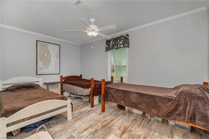 Bedroom with ceiling fan, ornamental molding, and light wood-type flooring