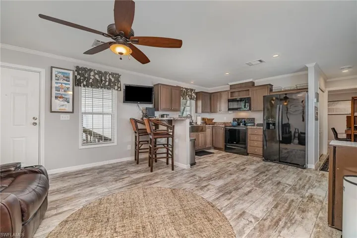 Kitchen with ornamental molding, a breakfast bar, light hardwood / wood-style flooring, and black appliances