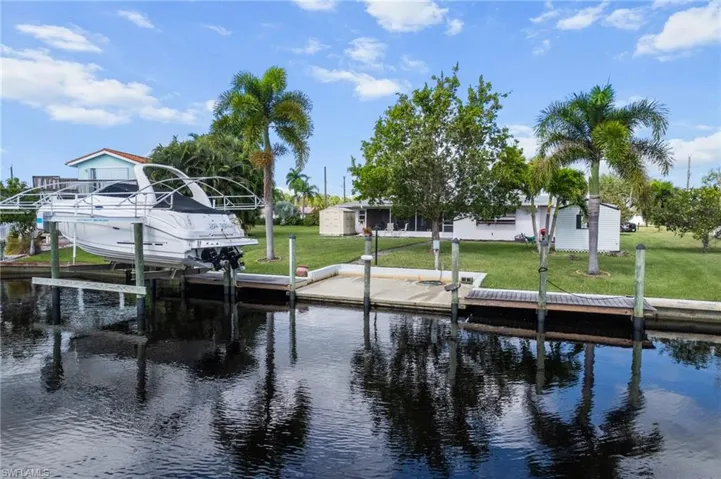 Dock area with a water view, boat lift, and a lawn