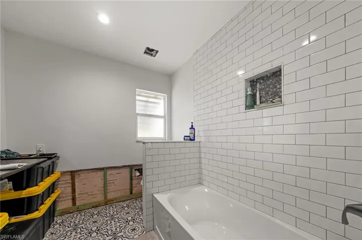 Full bath with tile walls, a garden tub, a wainscoted wall, light tile patterned floors, and recessed lighting