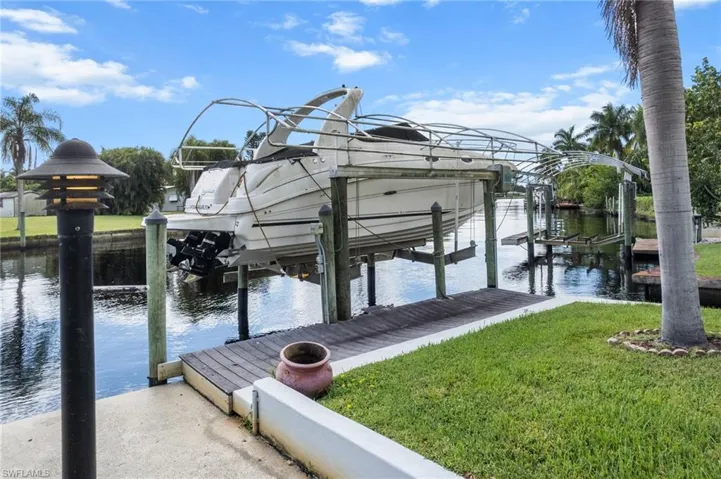 Dock area featuring boat lift, a water view, and a lawn
