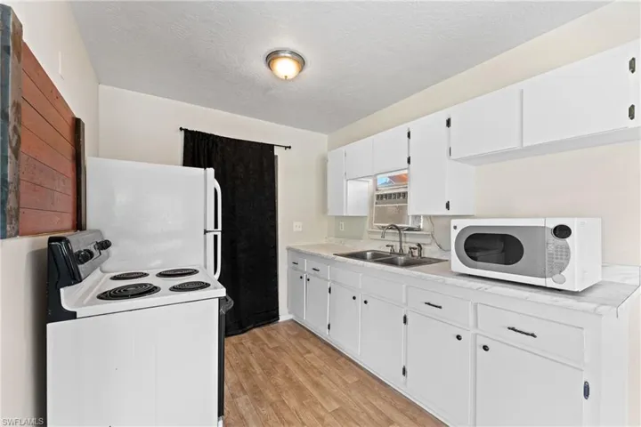 Kitchen featuring light wood-type flooring, a textured ceiling, white appliances, sink, and white cabinets