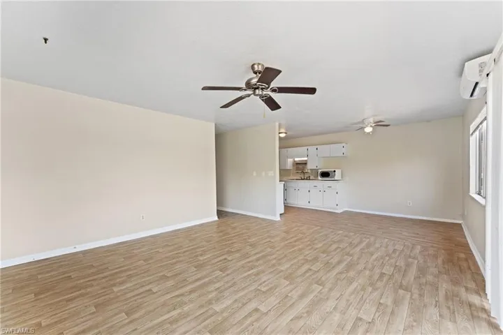 Unfurnished living room featuring an AC wall unit, ceiling fan, and light wood-type flooring