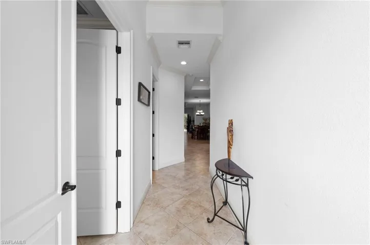 Hallway featuring neutral wall finishes, tile flooring, recessed lighting, crown molding, and white interior doors with dark hardware
