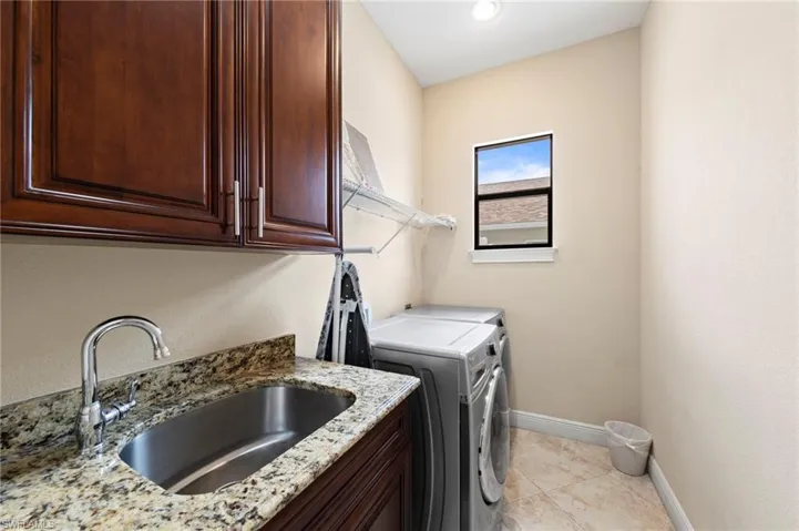 Laundry room featuring a stainless steel sink, granite countertop, rich wood cabinetry, tile flooring, and a window for natural light