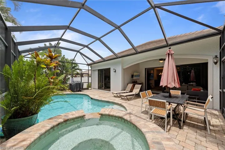 Screened lanai featuring a freeform pool, integrated hot tub with brick-finish coping, and ample paver patio space