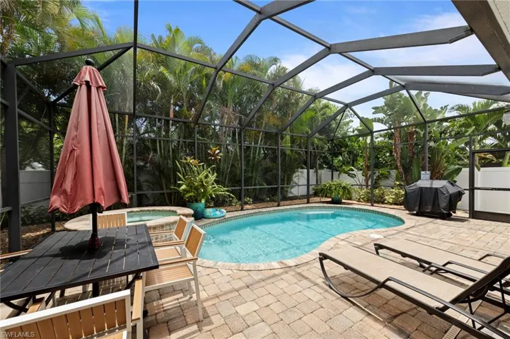 Screened enclosure featuring a freeform swimming pool with integrated spa, paver patio, and mature tropical landscaping