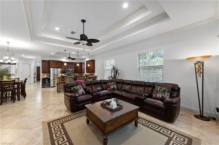 Expansive open-concept living area featuring tray ceilings with recessed lighting, tile flooring, and multiple windows with blinds