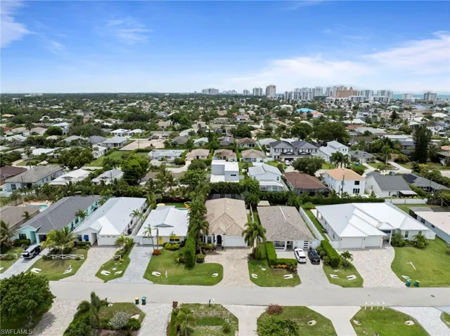 Aerial view showcasing this residential property's manicured landscape with mature trees, wide driveway, and concrete hardscaping