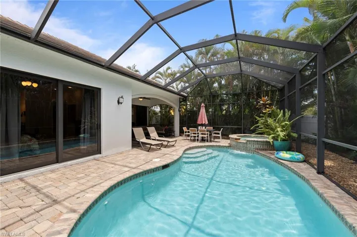 Screened-in pool area featuring a curved swimming pool, integrated spa with waterfall, spacious paver patio, covered lanai, and sliding glass doors
