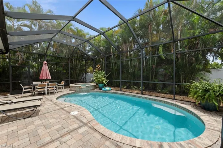 Screened pool enclosure featuring a freeform swimming pool, integrated spa, and paver patio