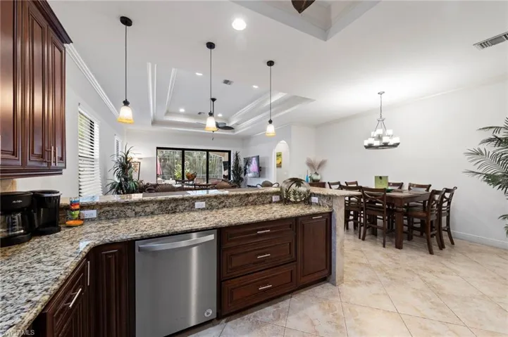 Kitchen area featuring stone countertops, dark wood cabinetry, a stainless steel dishwasher, and tile flooring