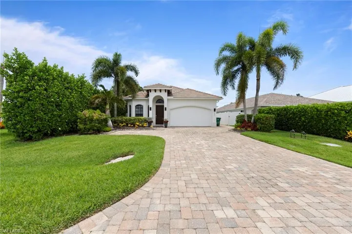 Front exterior featuring a white stucco facade, arched entryway, and a paver driveway