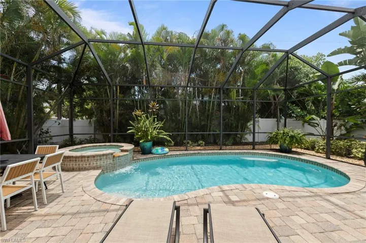 Resort-Style Screened Pool Oasis featuring a sparkling free-form saltwater pool with integrated sun shelf, surrounded by expansive pavers and mature tropical landscaping