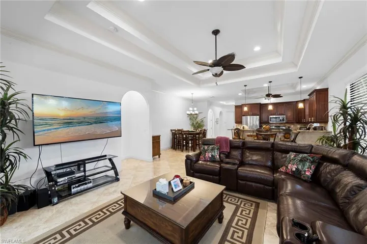 Open-concept living area featuring tray ceilings with crown molding, recessed lighting, and tile flooring