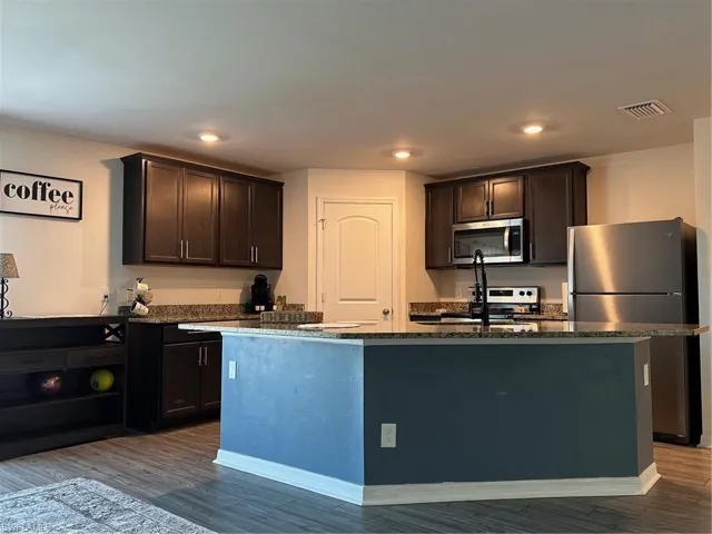 Kitchen featuring an island with sink, fridge, wood-type flooring, and dark brown cabinetry
