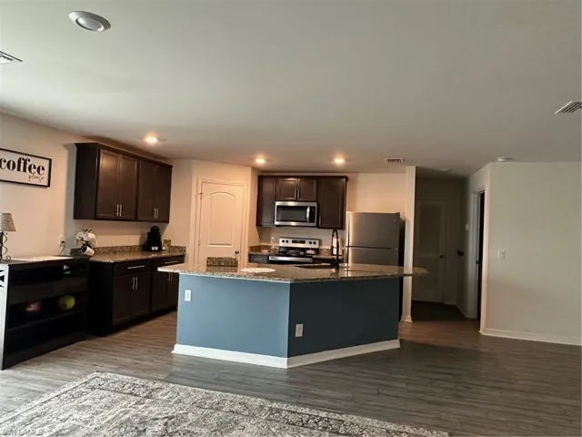 Kitchen with hardwood / wood-style flooring, a center island with sink, fridge, stove, and dark brown cabinetry