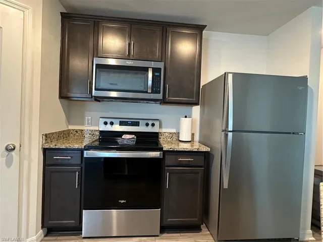 Kitchen with light stone counters, refrigerator, stove, and dark brown cabinetry