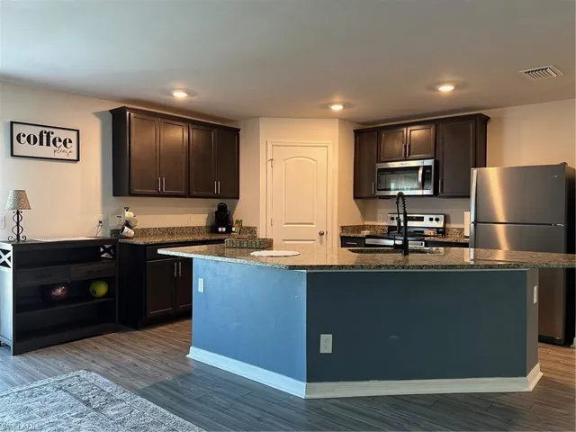 Kitchen featuring fridge, wood-type flooring, dark brown cabinets, and an island with sink