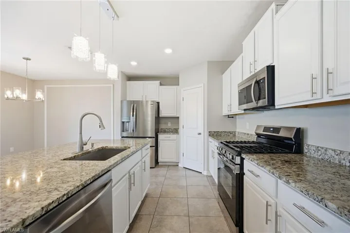 Kitchen featuring stainless steel appliances, white cabinetry, light stone countertops, light tile patterned floors, and suspended lighting