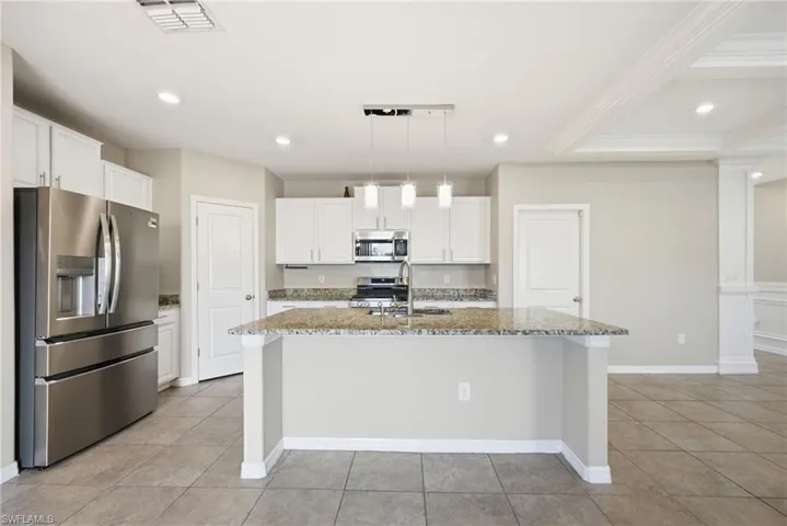 Kitchen with stainless steel appliances, light stone counters, white cabinets, hanging light fixtures, and a kitchen island with sink