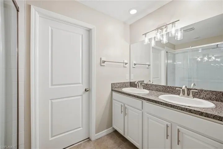 Bathroom featuring double vanity, a shower stall, and light tile patterned floors