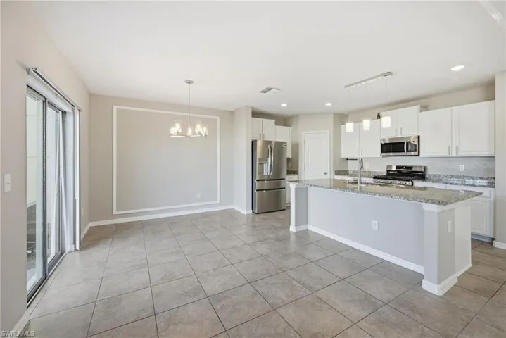 Kitchen with white cabinets, stainless steel appliances, light stone countertops, an island with sink, and a chandelier