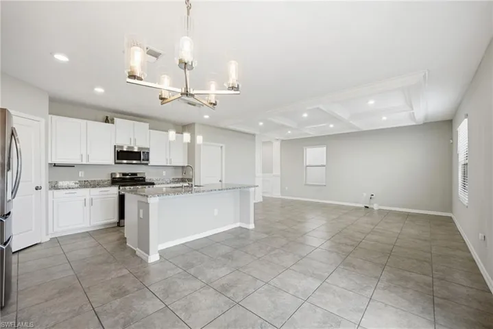 Kitchen with a kitchen island with sink, hanging lights, light stone counters, open floor plan, and stainless steel appliances