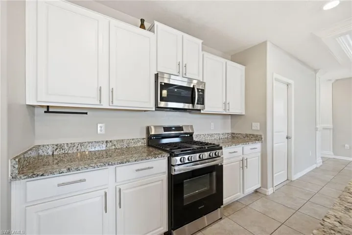 Kitchen with stainless steel appliances, white cabinetry, light stone countertops, and light tile patterned floors