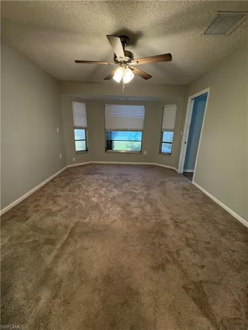 Carpeted empty room featuring a textured ceiling and ceiling fan